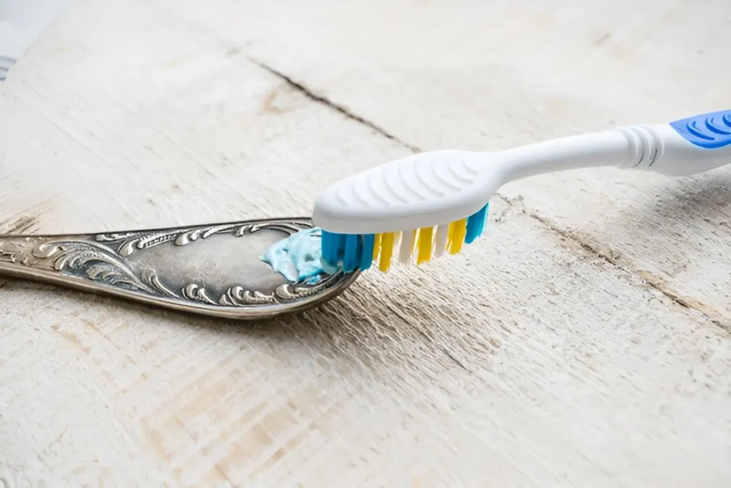 A flatware handle is being washed with toothpaste and tooth brush