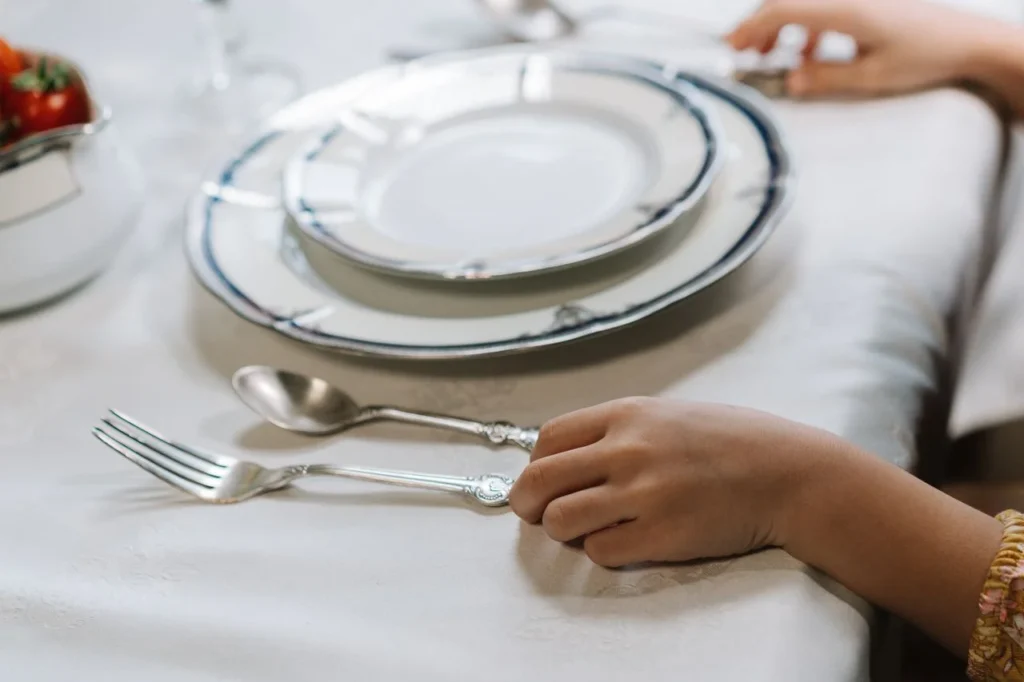 Two hands are ready to use a flatware set for a formal dinner