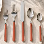 A 5 piece place setting of Mepra Fantasia flatware displayed on a napkin beside a dinner plate